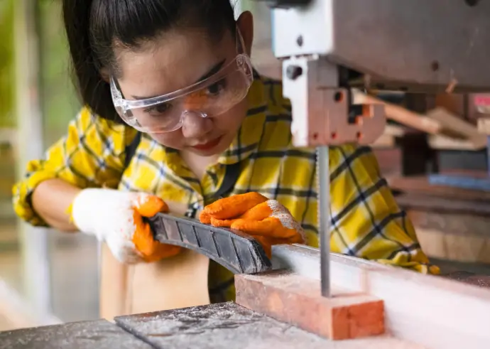 DIY hobby user cutting timber on a small wood bandsaw with safety glasses